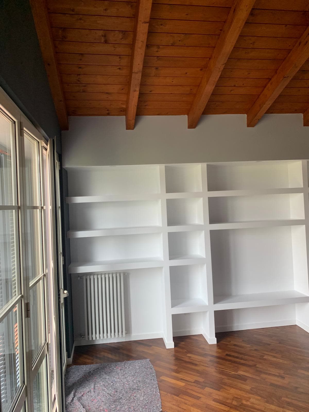 Soggiorno con libreria a muro su misura e tetto in travi di legno a vista, realizzato da Lotus Group